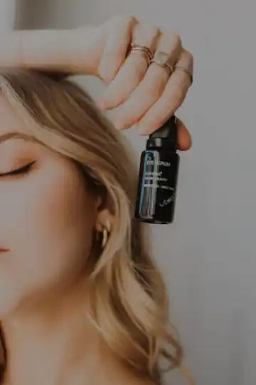 Dark glass dropper bottle being held near blonde hair.