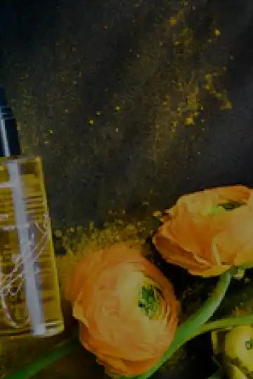 Delicate orange ranunculus flowers alongside a glass bottle.