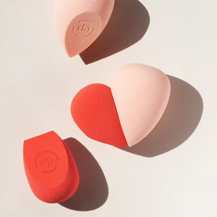 Makeup blending sponges in coral and pink tones casting shadows.