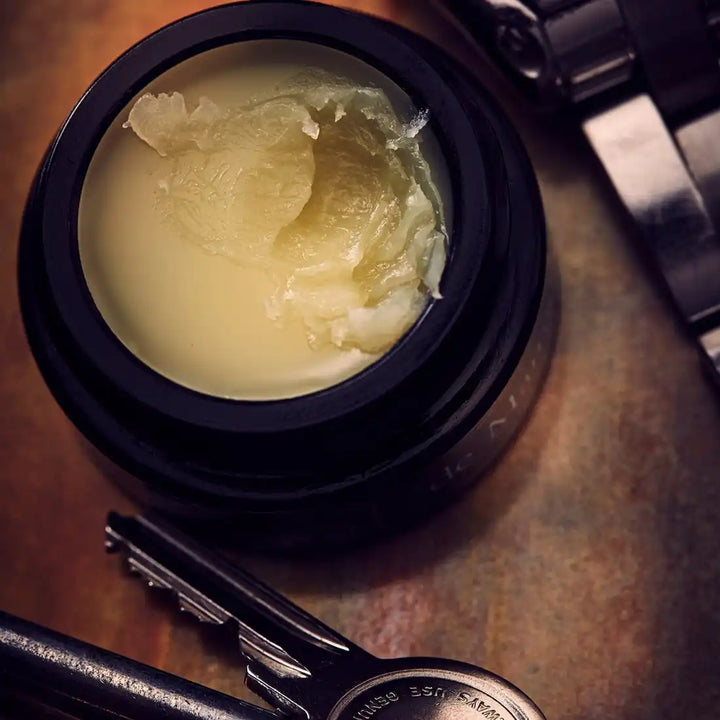 Open jar of hair pomade or styling wax with a creamy, pale yellow texture.