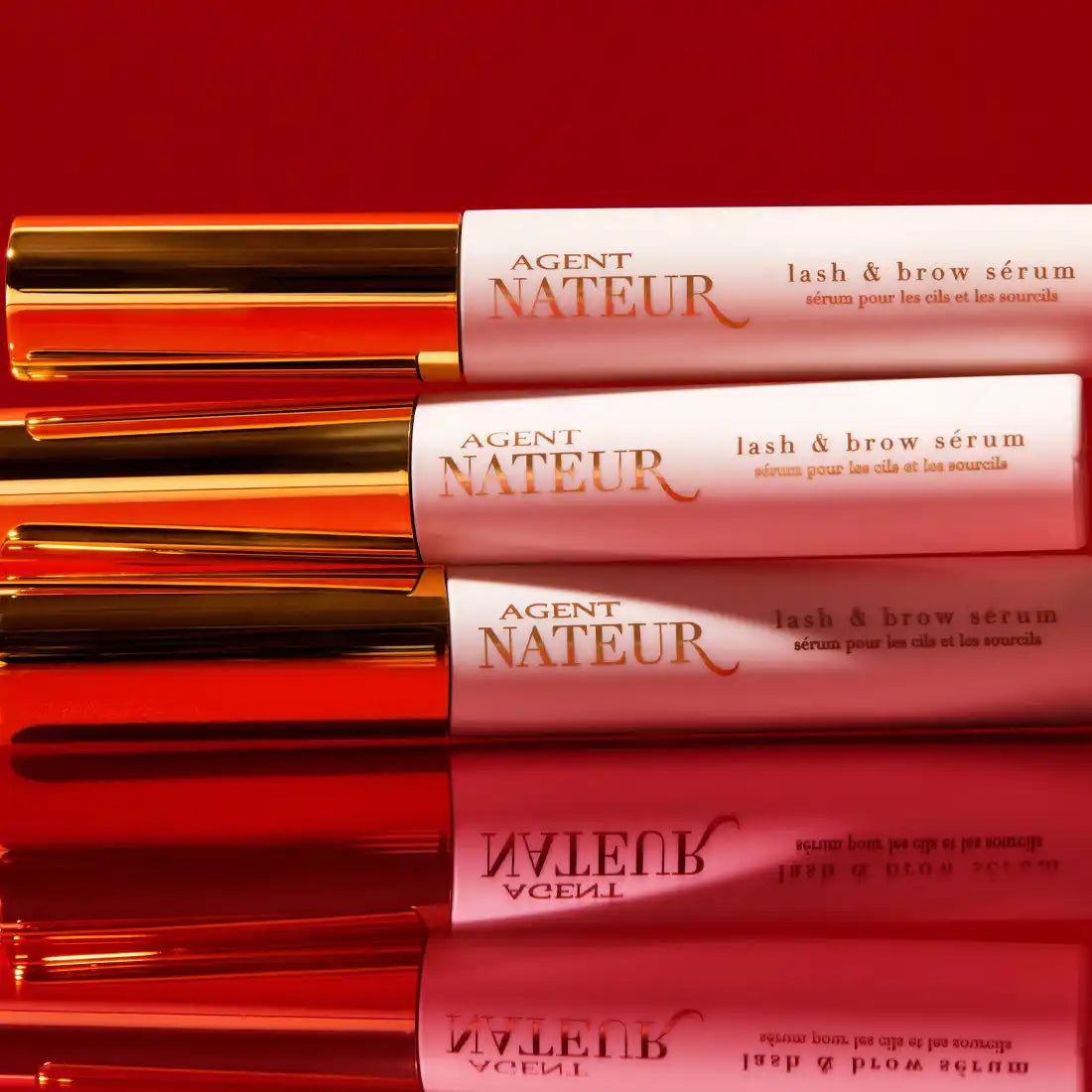 Pink and gold tubes of Agent Nateur lash and brow serum lined up in a row.