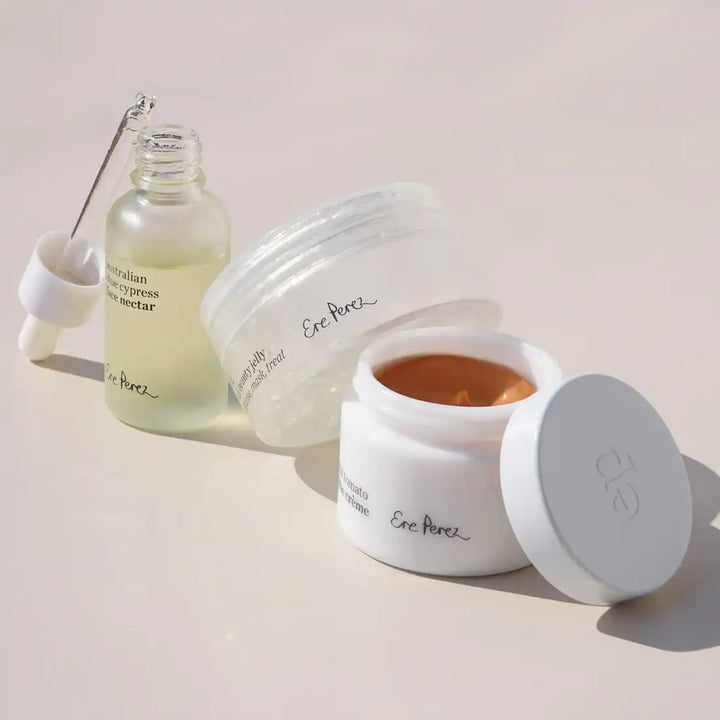 White cosmetic jar with a clear serum bottle and transparent disc beside it.